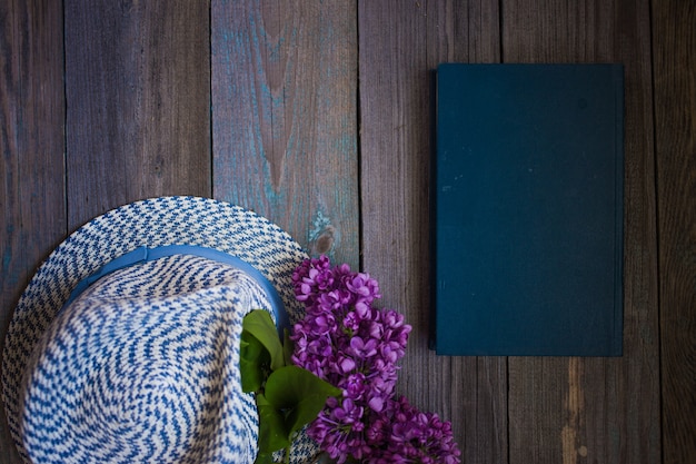 Branch of lilac, the hat and book on a wooden background