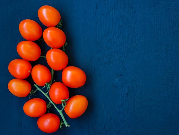 Branch of ripe cherry tomatoes on a blue wooden background place for your text