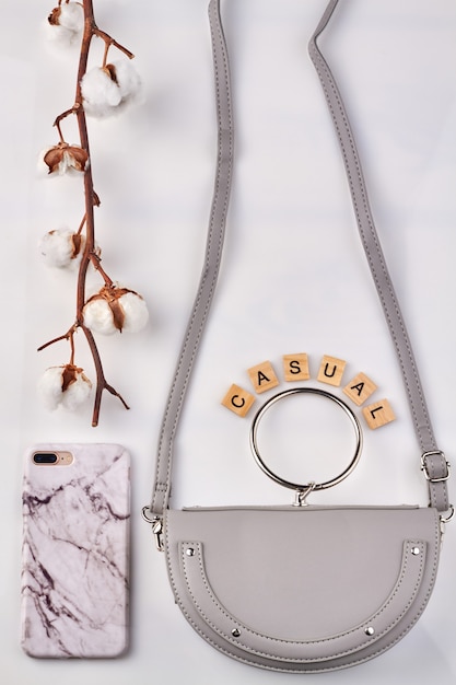 Photo branch of white cotton near fashionable things. stylish leather bag and marble phone case on white background.