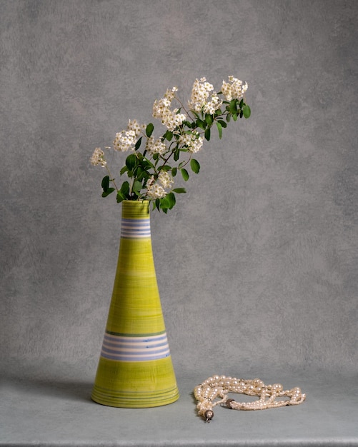 Photo branch with white flowers in a green vase on a gray background near white beads still life