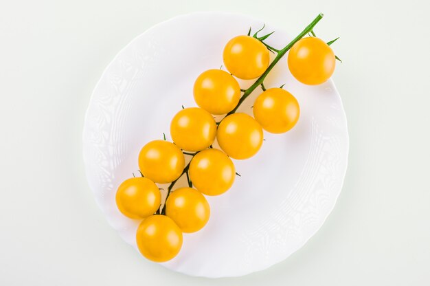 A branch of yellow cherry tomatoes on a white plate