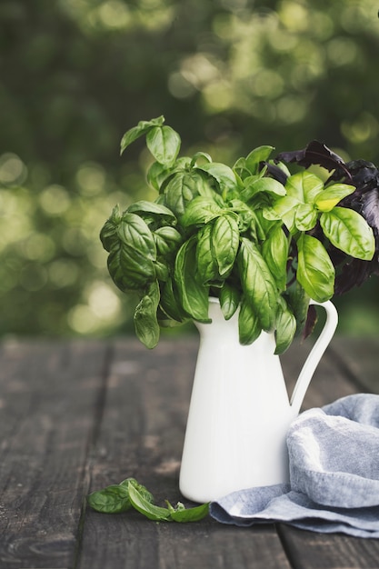 branches of basil in a jar on a table, against a backdrop of a garden