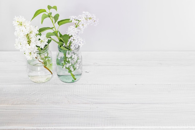 Branches of blooming multicolored lilac in glass jars on white wooden table