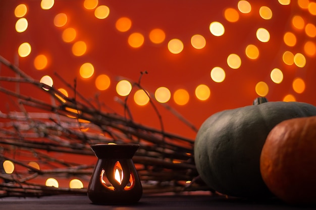 Branches, candle and pumpkins on an orange background with bokeh. Halloween. Copy space.