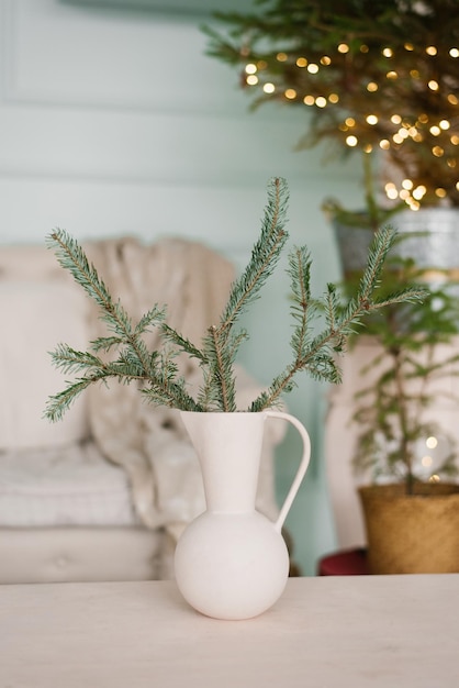 Branches of a Christmas tree in a white vase jug in the decor of the living room interior