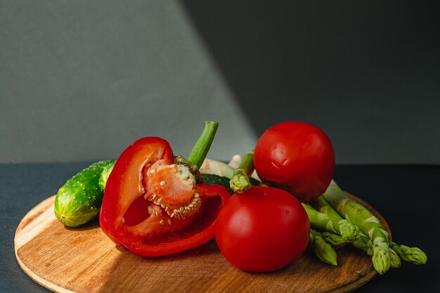 Photo branches of fresh green asparagus peppers tomatoes and cucumbers on a wooden board dark gray background top view basic trend concept with copy space