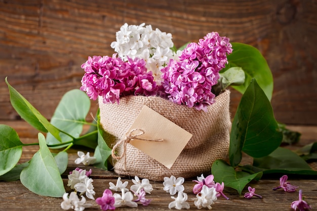 Branches of lilacs are in the basket of burlap on the surface of wooden boards