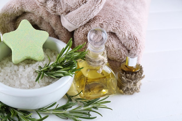 Branches of rosemary and sea salt towels candle and bottle with massage oil on color wooden background Rosemary spa concept