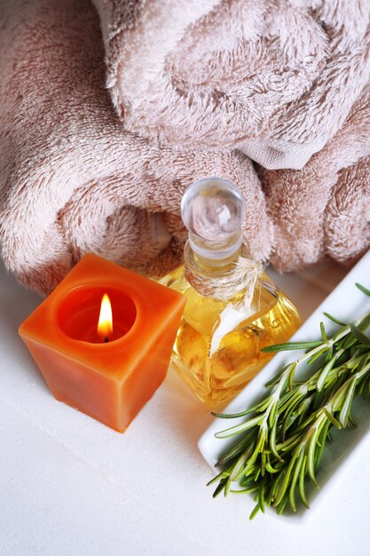 Branches of rosemary and sea salt towels candle and bottle with massage oil on color wooden background Rosemary spa concept