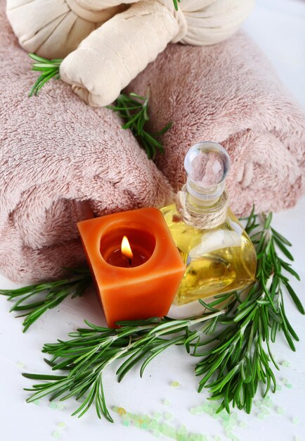 Branches of rosemary and sea salt towels candle and bottle with massage oil on color wooden background rosemary spa concept