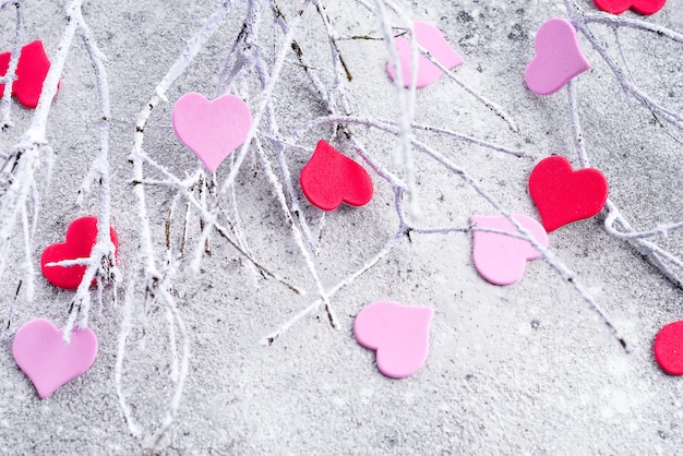 Branches in the snow with pink and red hearts on a concrete background 