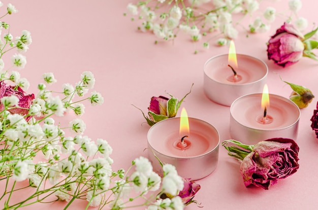 Brandende aromakaarsen met bloemen en gedroogde rozen op roze. SPA en aromatherapie concept.