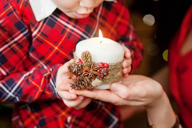 Brandende kaars in de handen van moeder en klein meisje. Kerst decor. Moeder en kind met mooie kaars met vuur. Kersttijd. Gelukkig gezin.