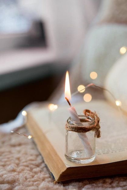 brandende kaars in een glazen pot op de achtergrond van een oud open boek. Vakantie bokeh lichten