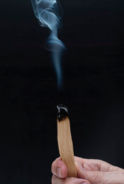Brandende stok van palo santo in handen op een zwarte achtergrond