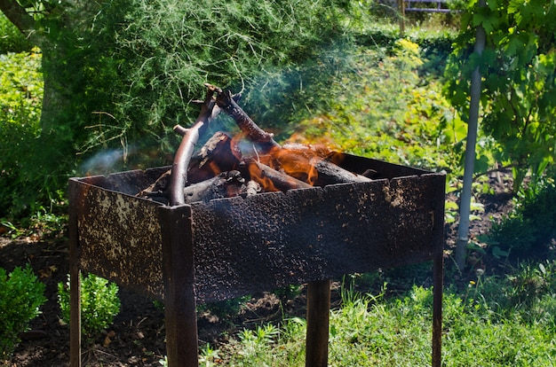 Brandhout branden in de barbecue. Vreugdevuur voor een picknick. Zonnige zomerdag buitenshuis.