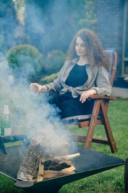 Brandhout in de grill buiten en intreepupil jonge vrouw met een glas limonade op achtergrond