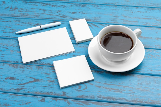 Branding briefpapier op blauw bureau. Bovenaanzicht van papier, visitekaartje, notitieblok, pennen en koffie.