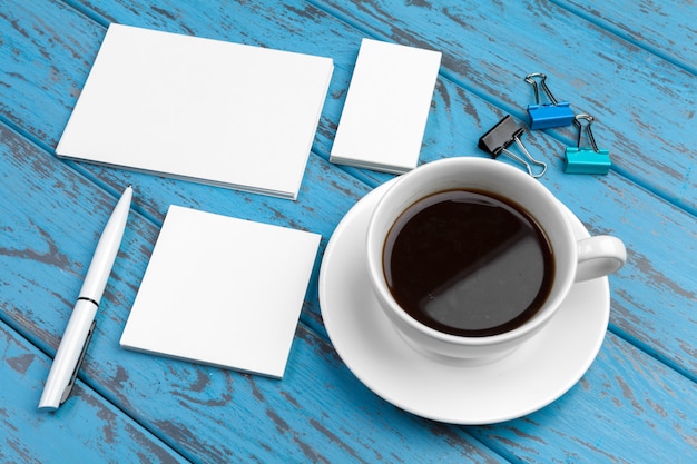 Branding briefpapier op blauw bureau. Bovenaanzicht van papier, visitekaartje, notitieblok, pennen en koffie.