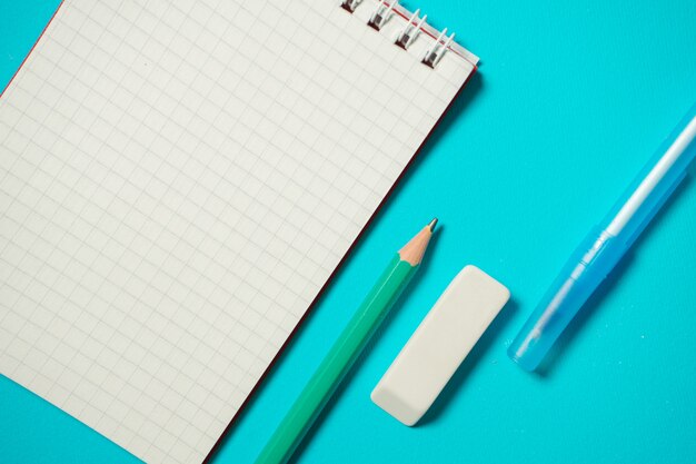 Branding mock up with pen, pencil, eraser and small notebook isolated on blue background. Copy space. Top view. Isometric concept. School supplies