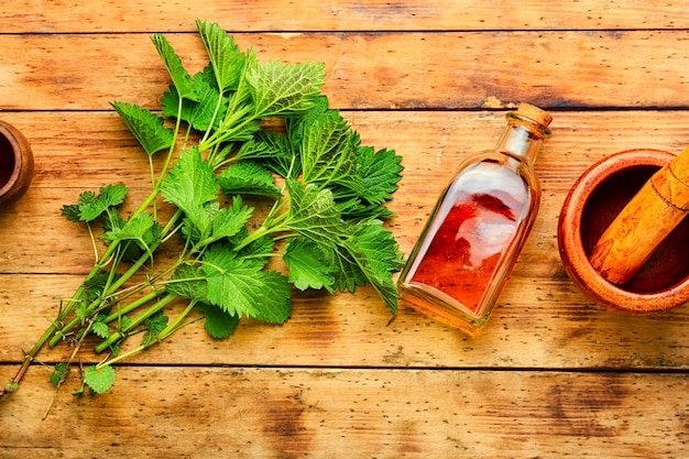 Brandnetelessentie in glazen fles en brandnetelbladeren op houten tafel. Brandnetels in de kruidengeneeskunde