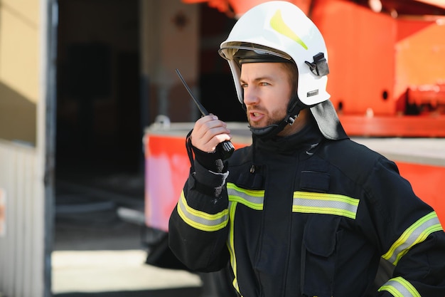 Brandweerman in een beschermend uniform staat naast een brandweerwagen en praat op de radio