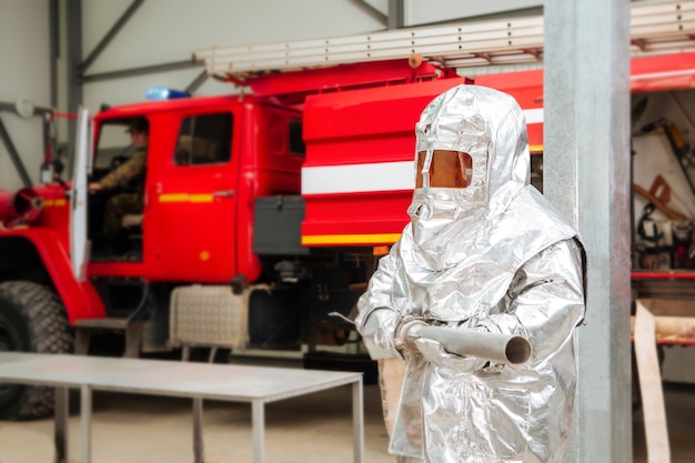 Brandweerman in een speciaal folie beschermend pak met een brandweerwagen op de achtergrond