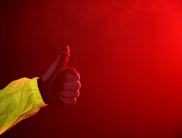 Brandweerman in handschoenen gebaren duim omhoog op een rode rokerige achtergrond