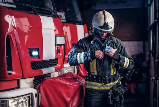 Brandweerman kleedt beschermende uniformen naast de brandweerwagen in de garage van een brandweer