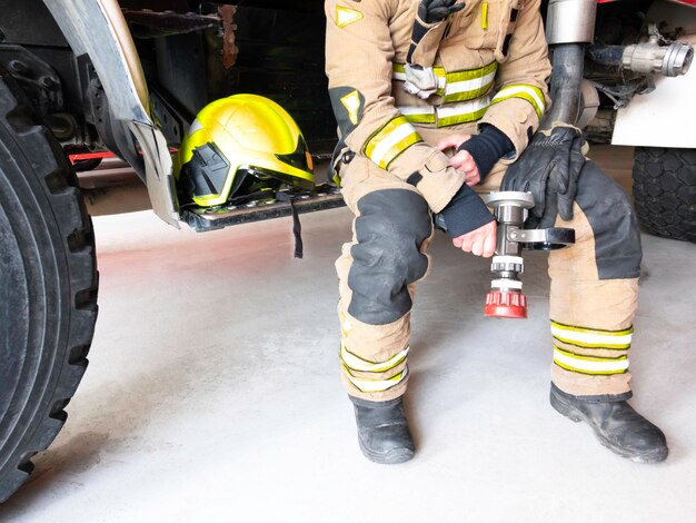 Foto brandweerman rust naast de vrachtwagen met helm en waterlans in de hand