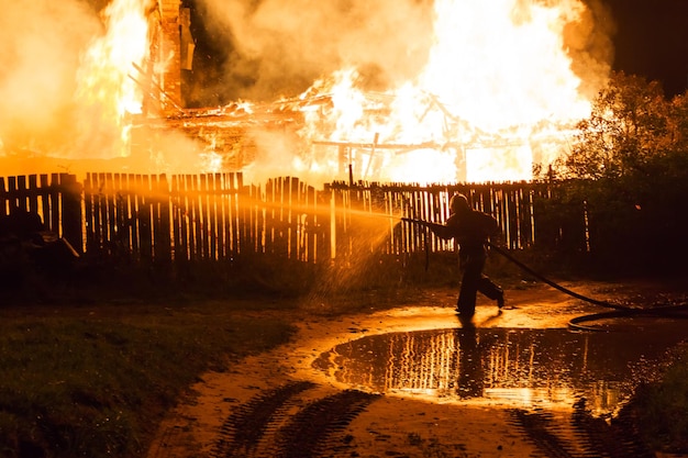 Brandweerman spuit water uit een slang op een brandend huis 's nachts