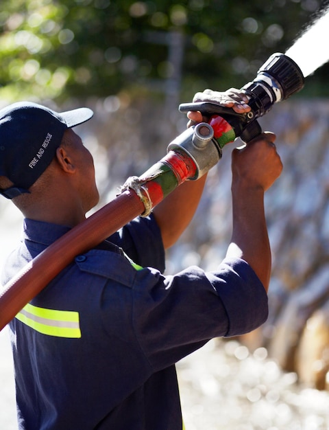 Brandweerman water en sproeislang voor noodhulp of brandbestrijding in de buitenlucht Brandweerman gebruikt grote vloeistofdrukleiding om buiten te spuiten of brand te blussen voor de veiligheid