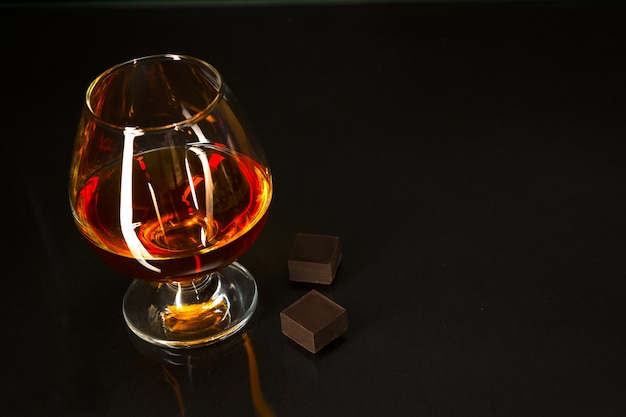 Foto bicchiere di brandy e cioccolato su sfondo nero