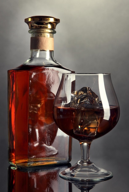 Brandy glass with ice and bottle on grey background