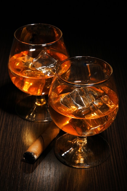 Brandy glasses with ice on wooden background