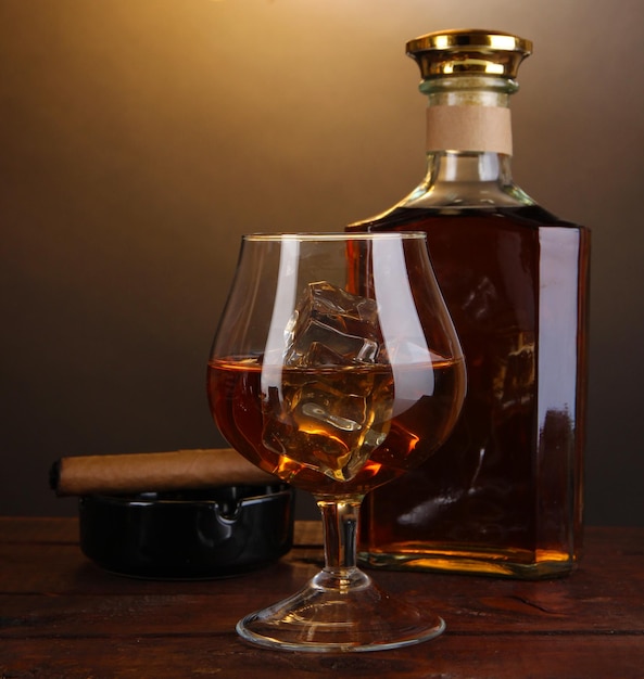 Brandy with ice on wooden table on brown background