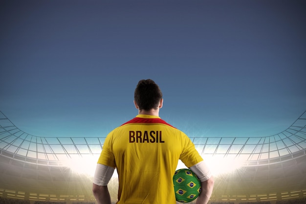 Brasil football player holding ball against large football stadium under blue sky