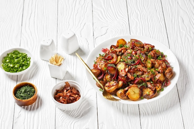 Bratkartoffelsalat geroosterde aardappelsalade met rode ui en spek op een witte plaat op een houten tafel Duitse keuken