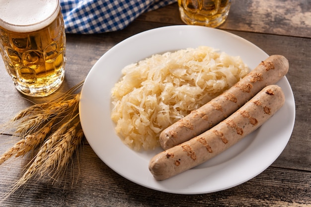 Фото Колбаса bratwurst, квашеная капуста, крендели и пиво на деревянном столе