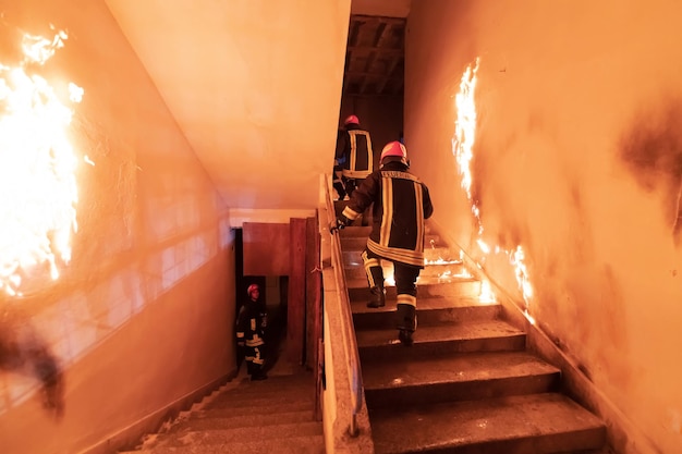 Brave Fireman Descends Stairs of a Burning Building and Holds Saved Girl in His Arms. Open fire and one Firefighter in the Background. High quality photo