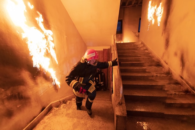 Brave Fireman Descends Stairs of a Burning Building and Holds Saved Girl in His Arms. Open fire and one Firefighter in the Background. High quality photo