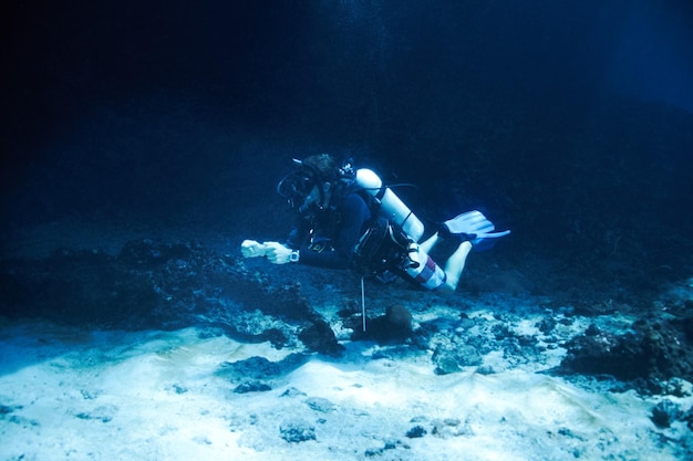 暗い海の深みに勇敢に立ち向かう海底のすぐそばに浮かぶオスのスキューバダイバー深海ダイビング