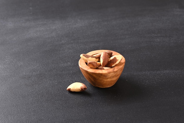 Photo brazil nut in woodenbowl on dark background