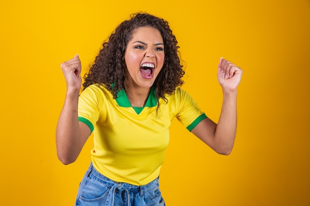 ブラジルのサポーター。サッカー、黄色の背景でサッカーの試合を祝うブラジルの巻き毛の女性ファン。ブラジルの色。