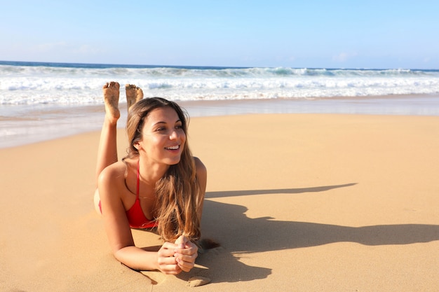 Braziliaans glimlachend mooi meisje dat op zand ligt dat van zon het looien zonnebaden genietend in zwempak