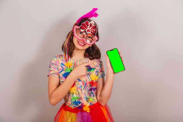 Braziliaans kindmeisje dat carnavalskleding draagt die het groene chromascherm van de smartphone laat zien en de close-upfoto van de mobiele telefoon laat zien