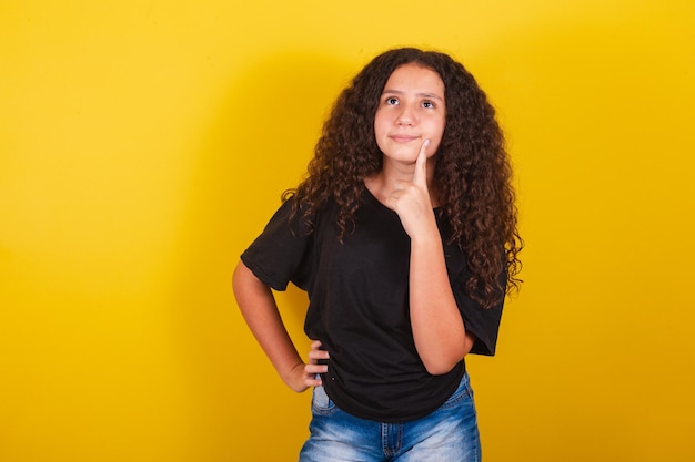 Braziliaans Latijns-Amerikaans meisje voor afro-haar gele achtergronduitdrukking van twijfel, denkende vinger op de wang