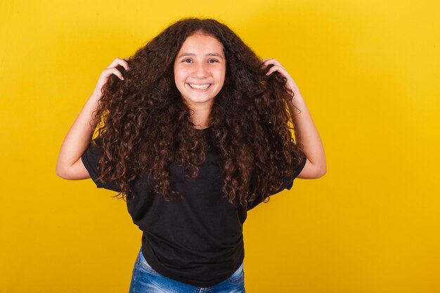 Braziliaans Latijns-Amerikaans meisje voor afrohaar gele achtergrond handen op haar hoofd haarsymbool krullend haar krullen gekapt haar mooi haar haarproducten