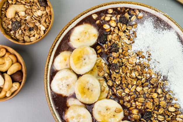 Braziliaanse acai in een witte kom met bananenpoeder, honing, muesli en noten in kleine bamboe kommen Cashewnoten en Para Bovenaanzicht Grijze achtergrond Selectieve focus