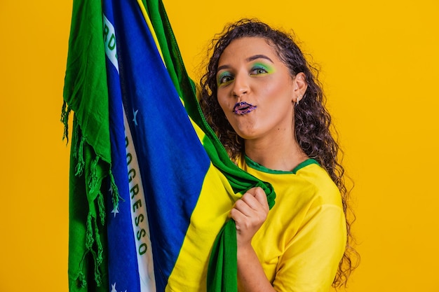 Foto braziliaanse fan met braziliaanse vlag in een portret braziliaanse fan die voetbal of voetbalwedstrijd viert op gele achtergrond kleuren van brazilworld cup
